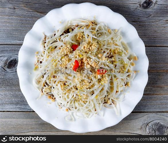 High angled view of Asian dish consisting of noodles, bamboo shoots, peppers and sesame seeds on rustic wood.