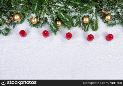High angled view of burning red candles, evergreen branches and gold colored ornaments covered in snow. Christmas concept with plenty of copy space.