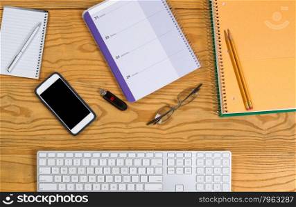 High angled view of desktop consisting of computer keyboard, pencils, pen, calendar, reading glasses, cell phone, notepad and thumb drive. Horizontal layout.