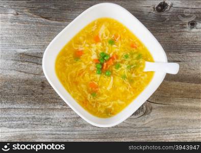 High angled view of egg and vegetable soup with spoon in bowl on rustic wood.