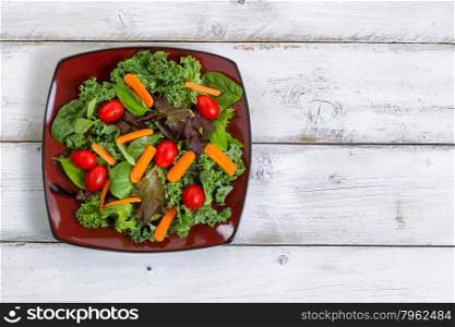 High angled view of fresh green salad with carrots, cherry tomato, basil, baby kale, and lettuce on rustic white wooden boards.