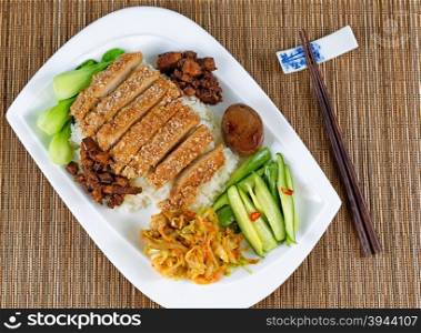 High angled view of fried bread coated pork with rice, egg and vegetables. Chopsticks in holder on bamboo mat.