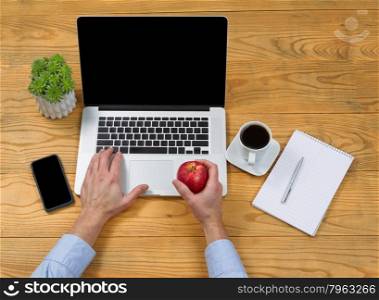 High angled view of male hand holding apple while typing on computer keyboard.&#xA;&#xA;