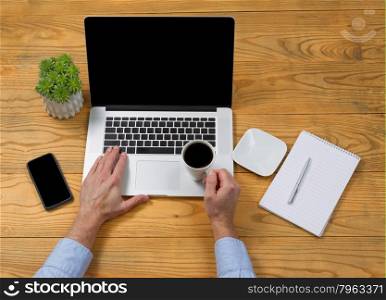 High angled view of male hand holding cup of coffee while typing on computer keyboard.