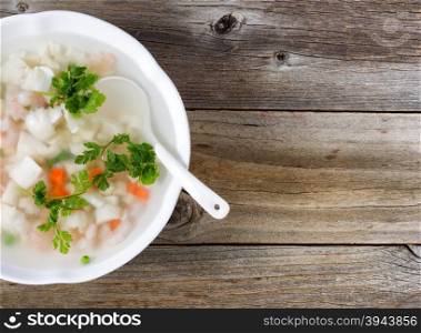 High angled view of seafood soup with spoon in bowl on rustic wood. Plenty of copy space on right side of image.