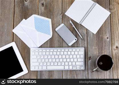High angled view of working desktop with cell phone, pen, paper, computer keyboard, coffee, envelopes, laptop and coffee. Concept of integrating tradition with modern technology.