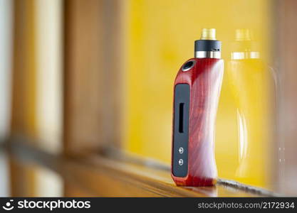 high end rebuildable dripping atomizer with red and black stabilized wood box mods on natural wood, yellow texture background, vaporizer equipment, selective focus