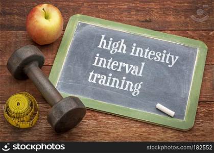 High intensity interval training  -  slate blackboard sign against rustic wood with a dumbbell, apple and tape measure