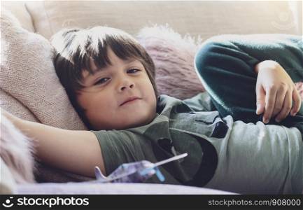 High key light happy boy lying on fluffy pillow on sofa, Selective focus Adorable child with smiling face relaxing at home on weekend, Warm and cozy scene in Pastel tone,