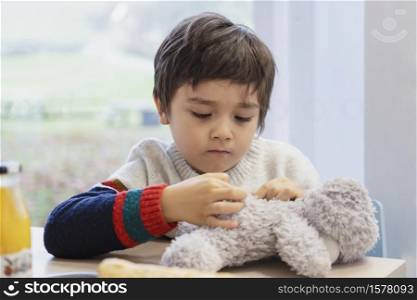High key light portrait cute boy plying teddy bear on table, Adorable Child playing with toys and relaxing while waiting for food in cafe.