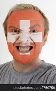 High key portrait of an angry man whose face is painted in colors of swiss flag