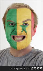 High key portrait of an angry man whose face is painted in colors of senegal flag