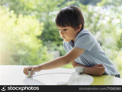 High key portrait of school kid playing game in playroomwith blurry natural background, Child holding bottom game with wondering face in a sunny room next to window, Learn and play, Education concept