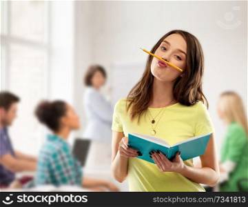 high school, education and people concept - foolish teenage student girl in yellow t-shirt with diary or notebook and pencil-mustache over classroom and teacher background. teenage student girl with notebook at school
