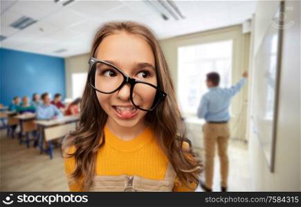 high school, education and people concept - smiling teenage student girl in glasses over classroom background. smiling teenage student girl in glasses at school