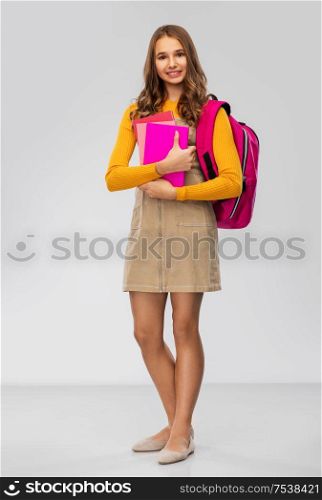 high school, education and people concept - smiling teenage student girl with backpack and books over grey background. teenage student girl with backpack and books
