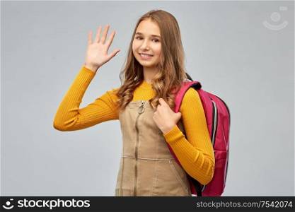 high school, education and people concept - smiling teenage student girl with backpack waving hand over grey background. smiling teenage student girl with backpack