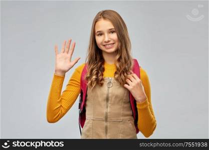 high school, education and people concept - smiling teenage student girl with backpack waving hand over grey background. smiling teenage student girl with backpack