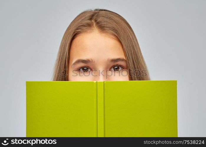 high school, education and people concept - teenage student girl hiding over book on grey background. teenage student girl hiding over book