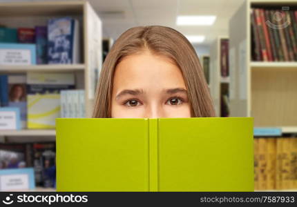 high school, education and people concept - teenage student girl hiding over book on library background. teenage student girl hiding over book at library