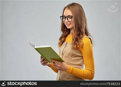 high school, education and vision concept - smiling teenage student girl in glasses reading book over grey background. teenage student girl in glasses reading book