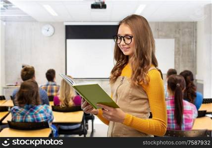 high school, education and vision concept - smiling teenage student girl in glasses reading book over classroom background. student girl in glasses reading book at school
