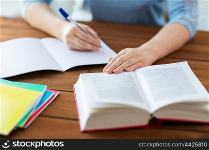 high school, education, people and learning concept - close up of young student or woman with book writing to notebook at home
