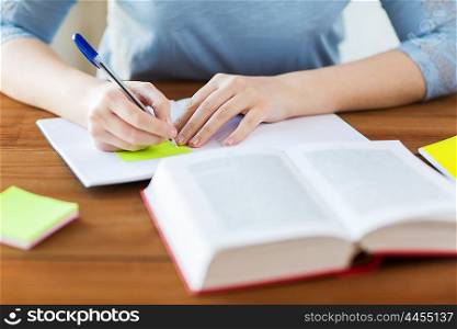 high school, education, people and learning concept - close up of young student or woman with book and notebook writing on sticker at home