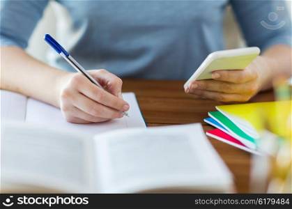 high school, education, people and learning concept - close up of young student or woman with smartphone and book writing to notebook at home