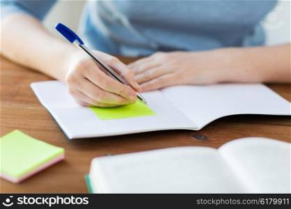 high school, education, people and learning concept - close up of young student or woman with book and notebook writing on sticker at home