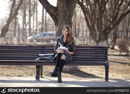 High school schoolgirl sitting on a bench with a notebook in the spring park
