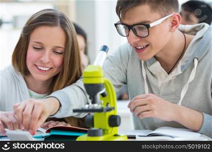 High School students. Girl and boy working together at biology classroom: choosing a biological sample on glass to look through microscope