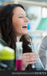 High School students. Pretty female student laughing while mixing reagents using glassware in classroom environment