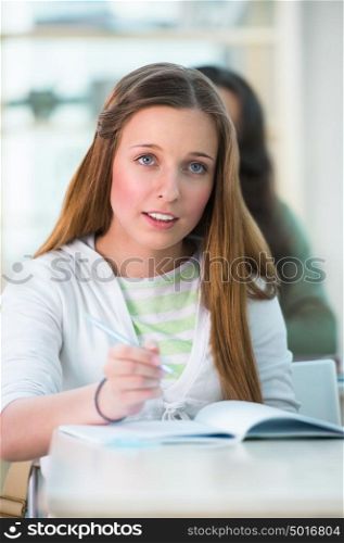 High School students. Pretty female student making notes in classroom during lecture