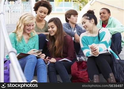 High School Students Sitting Outside Building With Phones