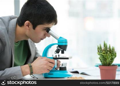 High School students. Young handsome male student looking through microscope biological sample in science classroom