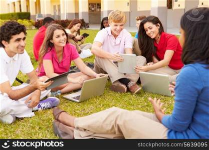 High School Teacher Sitting Outdoors With Students On Campus