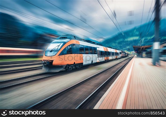 High speed orange train in motion on the railway station at sunset. Modern intercity passenger train with motion blur effect on the railway platform. Industrial. Railroad in Europe. Transport. High speed orange train in motion on the railway station