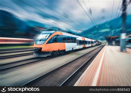 High speed orange train in motion on the railway station at sunset. Modern intercity passenger train with motion blur effect on the railway platform. Industrial. Railroad in Europe. Transport. High speed orange train in motion on the railway station