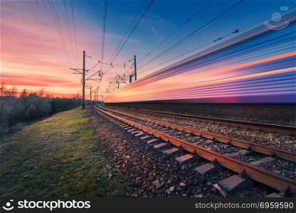 High speed passenger train in motion on railroad at sunset. Blurred modern commuter train. Railway station and colorful sky. Railroad travel, railway tourism. Industrial landscape. Transportation. High speed passenger train in motion on railroad