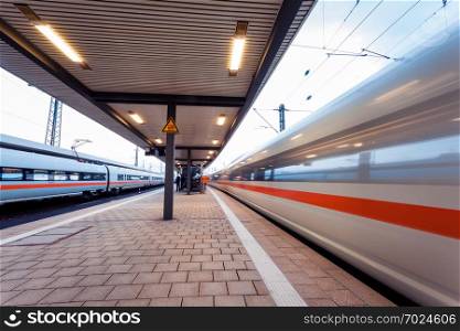 High speed passenger train on railroad track in motion at sunset. Blurred commuter train. Railway station in Nuremberg, Germany. Industrial landscape