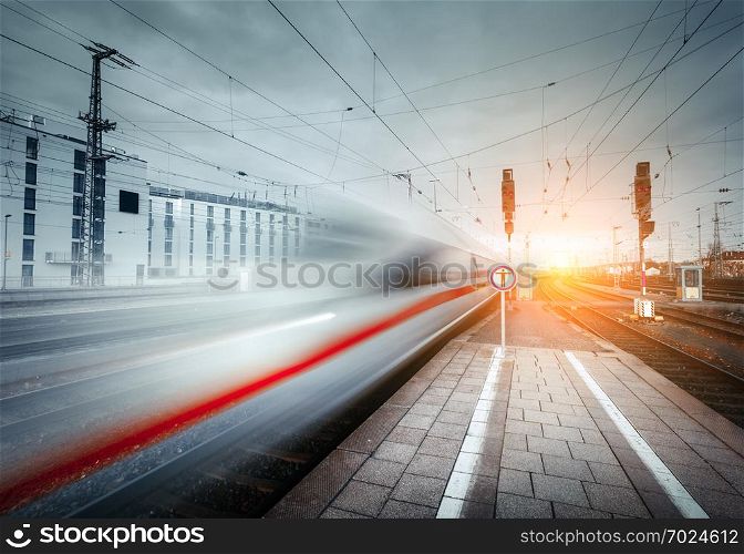High speed passenger train on railroad track in motion at sunset. Blurred commuter train. Railway platform in the city. Railway station in Europe. Railroad with vintage toning. Industrial landscape