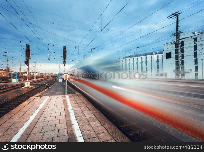 High speed passenger train on railroad track in motion. Blurred commuter train. Railway platform in the city. Railway station in Europe. Railroad with vintage toning. Industrial concept landscape