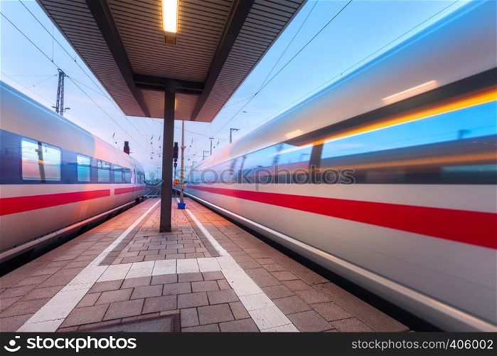 High speed passenger trains on railroad platform in motion at dusk. Blurred train. Railway station at night in Nuremberg, Germany. Railroad travel, railway tourism. Industrial landscape. Transportation