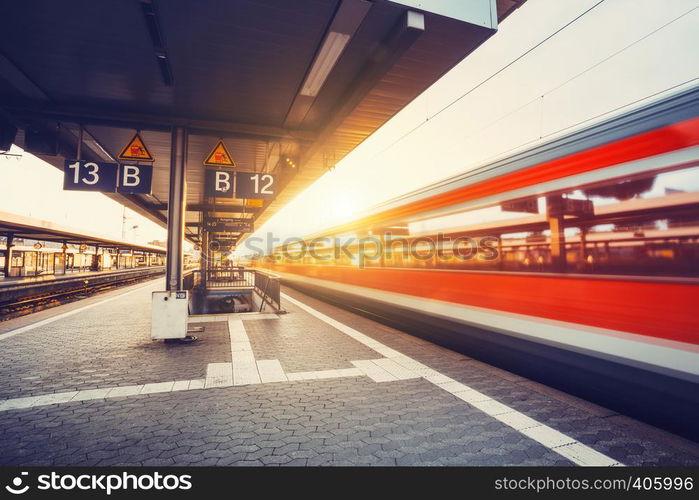 High speed red passenger train in motion at railway platform at sunset. Blurred commuter train. Railway station. Railroad travel, railway tourism. Industrial landscape. Vintage toning. Instagram style