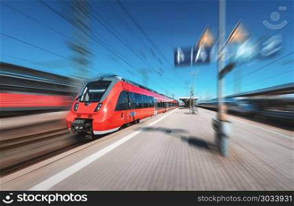 High speed red train in motion on the railway station at bright day. Modern intercity train with motion blur effect on the railway platform. Industrial. Passenger commuter train on railroad. Travel. High speed red train in motion on the railway station