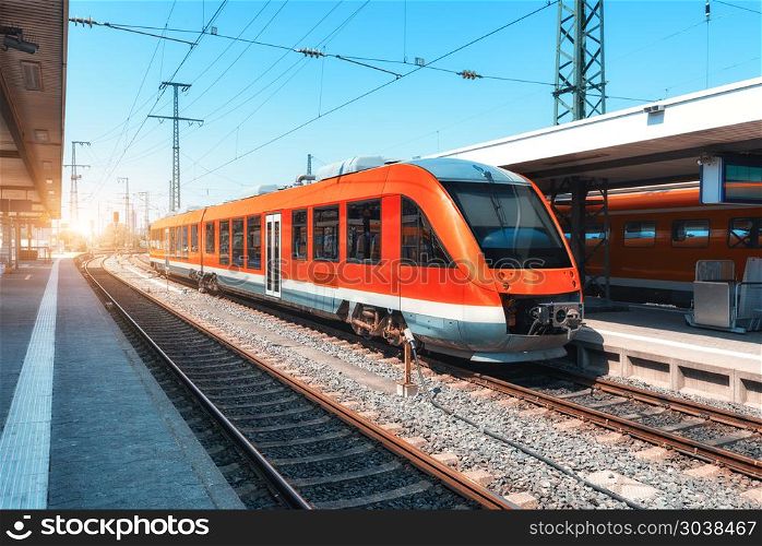 High speed red train on the railway station at sunset in summer. Modern commuter train on the railway platform. Industrial scene with railroad. Passenger transportation. intercity vehicle. Travel. High speed train on the railway station at sunset in summer