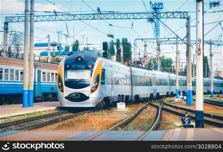 High speed train arrives on the railway station at sunset in Europe. Modern intercity train on the railway platform. Industrial landscape with passenger train on railroad. Railway transportation. High speed train arrives on the railway station