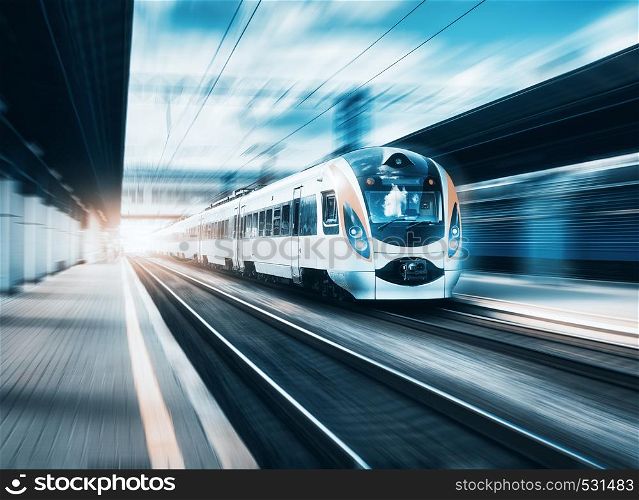 High speed train at the railway station at sunset in Europe. Modern intercity train on railway platform. Urban scene with beautiful passenger train on railroad and buildings. Railway landscape