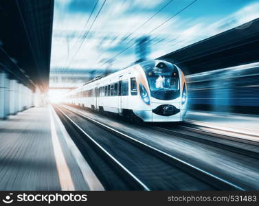 High speed train at the railway station at sunset in Europe. Modern intercity train on railway platform. Urban scene with beautiful passenger train on railroad and buildings. Railway landscape